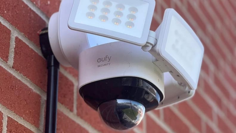 White surveillance system with built-in cameras and lights mounted on a brick wall.