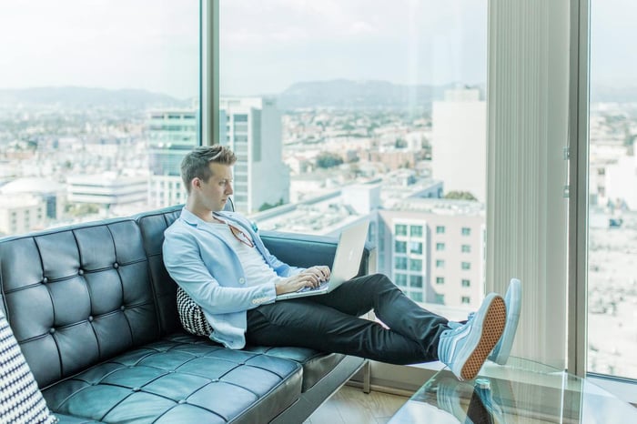 A man working on a laptop on a sofa with the view of the city